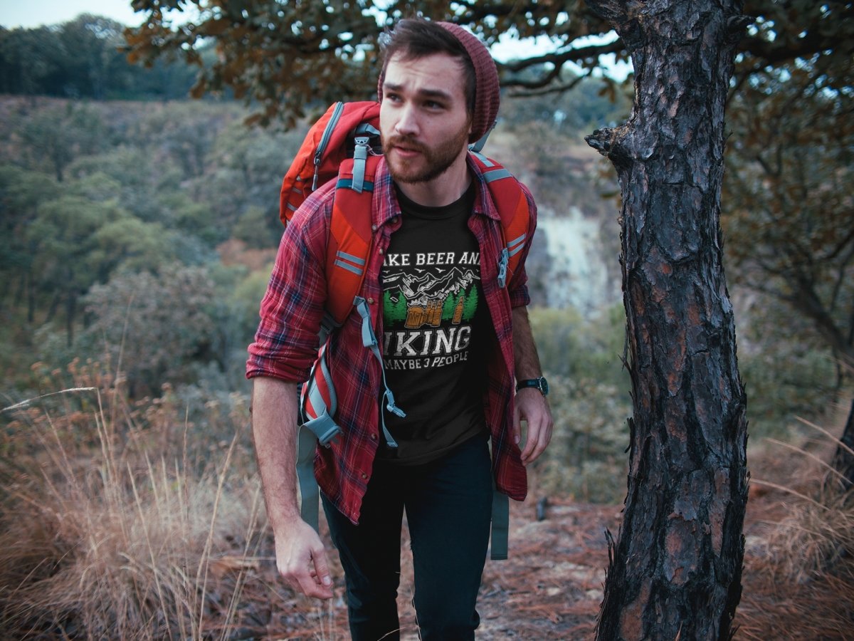 Ein Mann, der mit einem Hoppymerch-Rucksack „I Like Beer, Hiking and Maybe 3 People“ Bier T-Shirt für Männer durch den Wald geht.