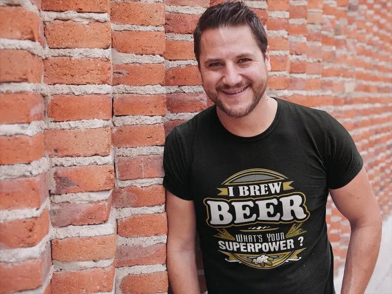 Ein Mann trägt ein Hoppymerch-Bio-T-Shirt mit der Aufschrift „Ich braue Bier. Was ist deine Superkraft?“